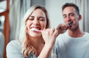 мъж и жена мият зъби с четки